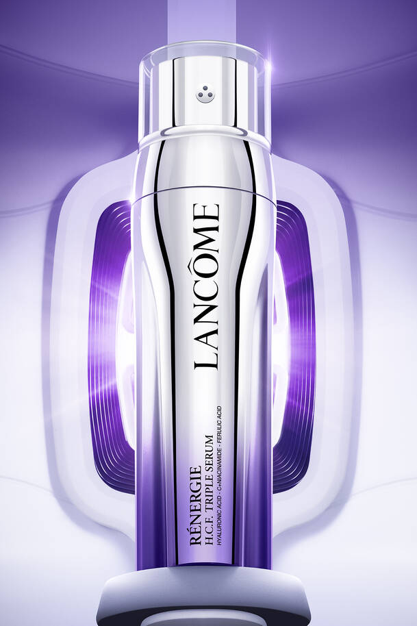 מוצרי איפור וטיפוח מבית לנקום (Lancome) מעוצבים על חול ים תחת שמיים בהירים, כולל מסקרה Lash Idole Curl Goddess בגוון זהב-ורוד, שפתוני Cheeks Juicy Tubes, ומייק-אפ קומפקט לצד מגבת ורודה.